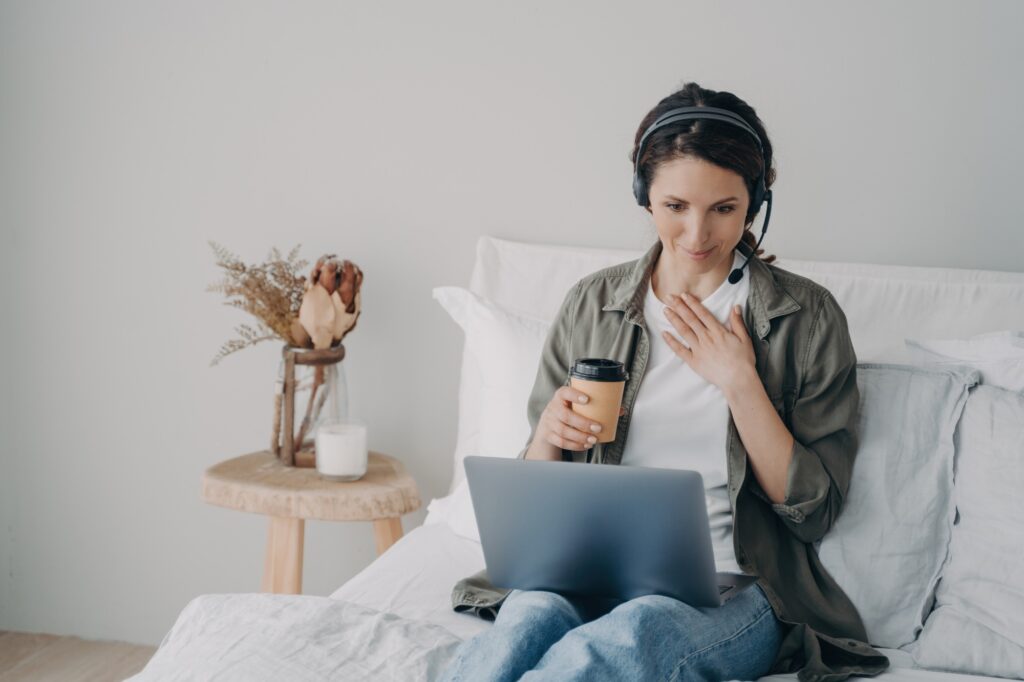 Woman life coach in headset conducts online consultation by video call on laptop in bedroom at home